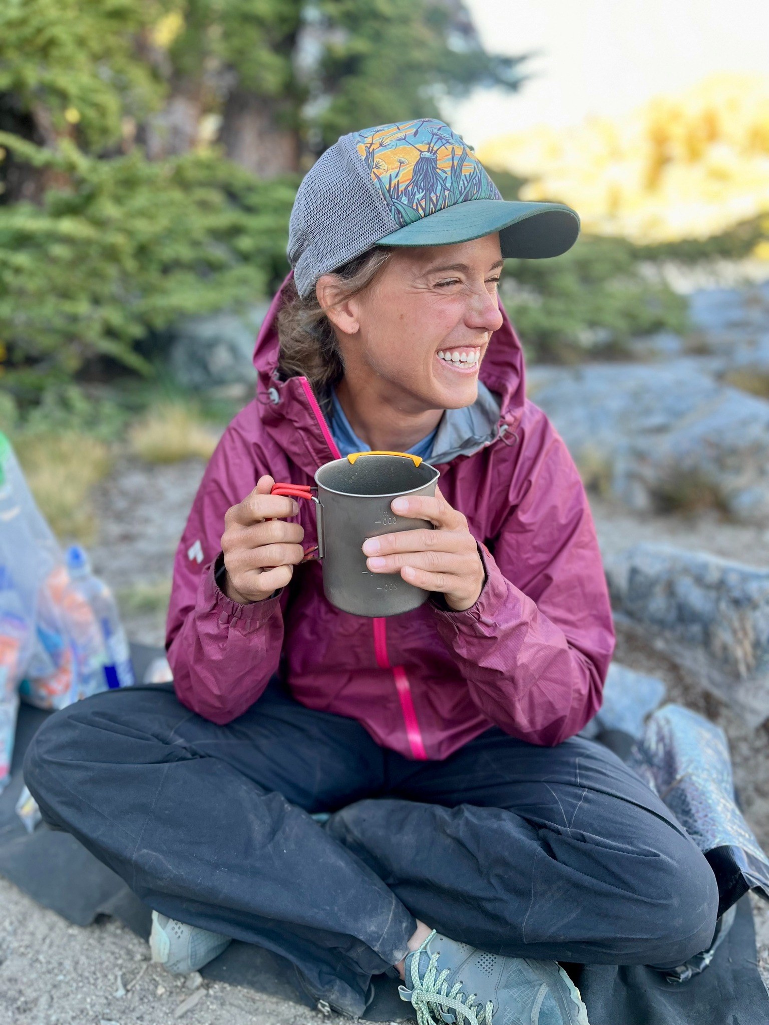 Sasha smiling while holding a camp mug outdoors