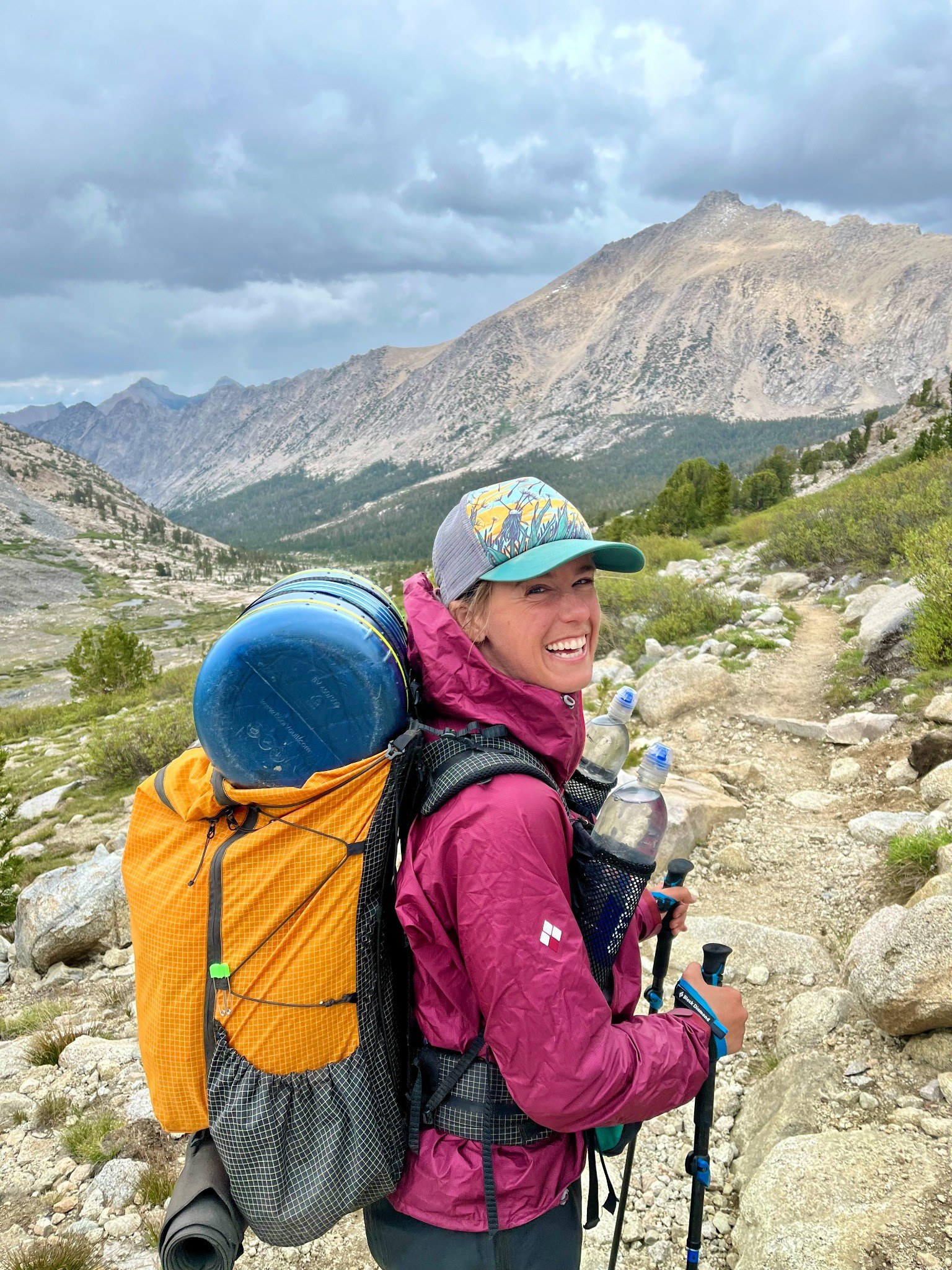Sasha smiling back on a mountain trail with a backpack