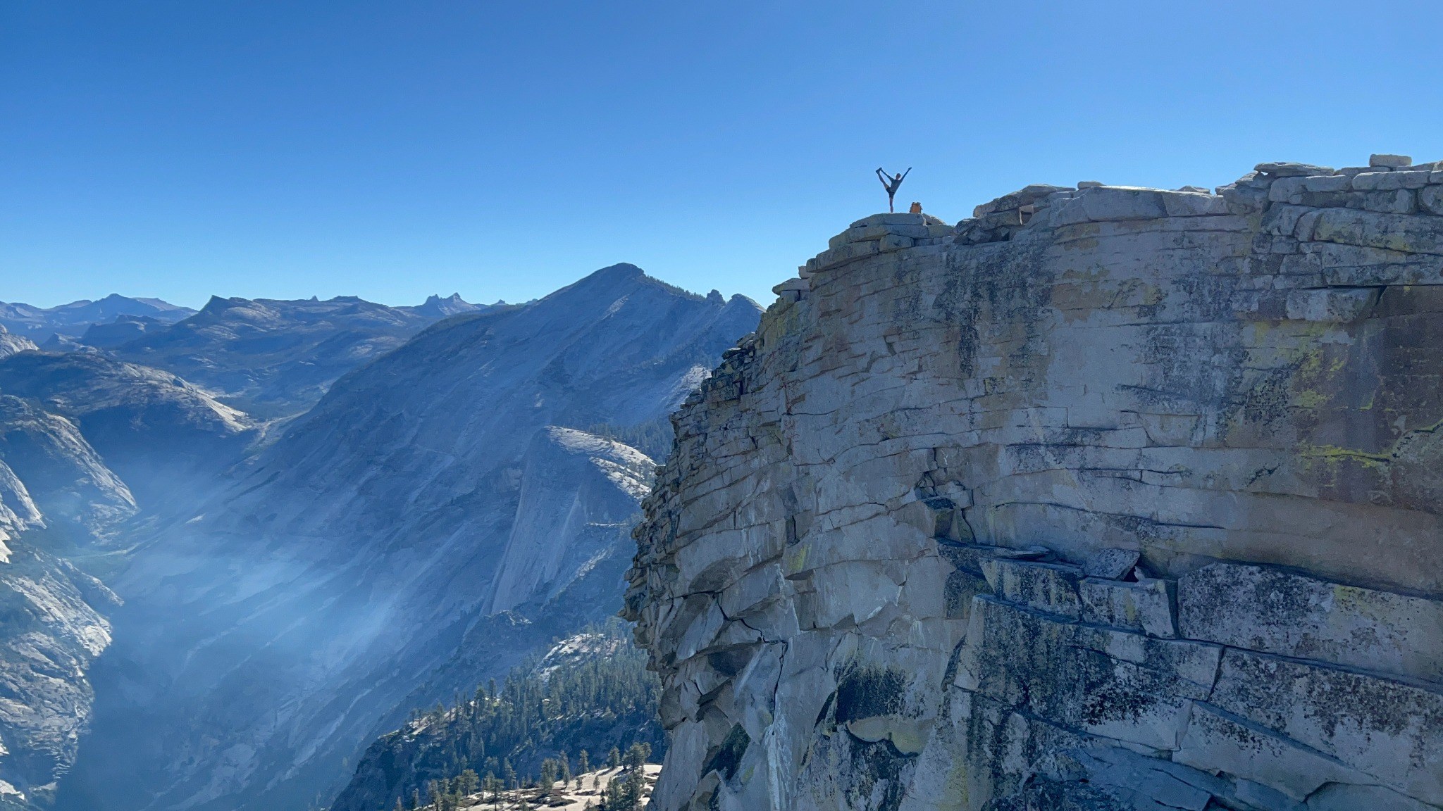 A small silhouette standing on a large cliff above mountain terrain