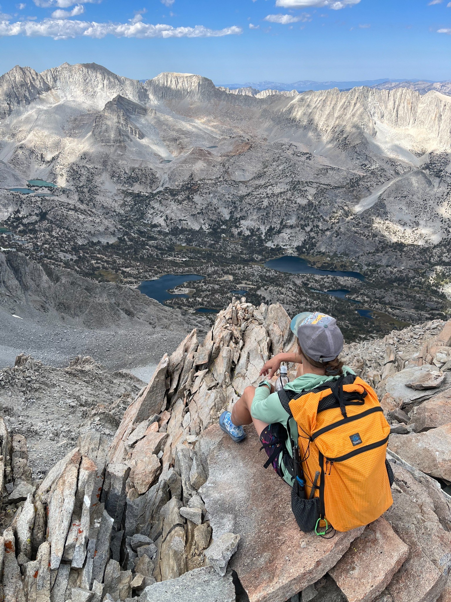 Sasha sitting on a mountain summit looking over alpine lakes